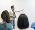 A man in a blazer gives a presentation to a captivated audience in a lecture setting.